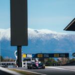 Circuitul de Formula 1 din Barcelona în timpul unei sesiuni de teste, cu mașini de curse pe pistă și infrastructura specifică competițiilor auto.