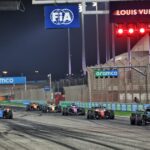Startul unei curse de Formula 1 pe un circuit nocturn, cu mașini aliniate și pregătite pentru competiție, sub sigla FIA și în prezența sponsorilor oficiali.