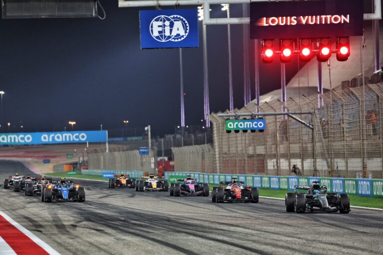 Startul unei curse de Formula 1 pe un circuit nocturn, cu mașini aliniate și pregătite pentru competiție, sub sigla FIA și în prezența sponsorilor oficiali.
