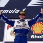 Damon Hill pe podiumul Formulei 1 alături de echipa Williams, înconjurat de logo-urile Shell și Rothmans, într-o fotografie din anii '90.