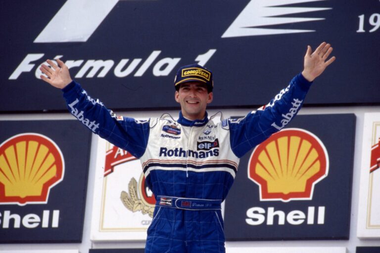 Damon Hill pe podiumul Formulei 1 alături de echipa Williams, înconjurat de logo-urile Shell și Rothmans, într-o fotografie din anii '90.
