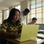 Studenți lucrând pe laptopuri Apple, inclusiv MacBook Neo, într-o sală de clasă luminoasă.