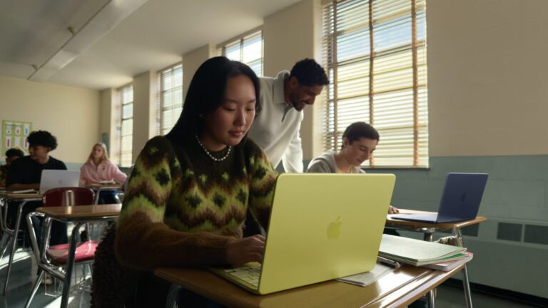 Studenți lucrând pe laptopuri Apple, inclusiv MacBook Neo, într-o sală de clasă luminoasă.